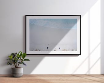 Könnte beinhalten: Gerahmte Luftaufnahme einer Strandszene mit schwarzem Rahmen. Das Foto zeigt einen hellblauen Ozean, der auf einen weißen Sandstrand trifft. Das Bild wird an einer weißen Wand mit einer Topfpflanze auf einer Holzoberfläche angezeigt.