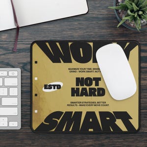 Peut inclure: Tapis de souris rectangulaire avec un fond doré et du texte noir qui dit "WORK SMART, NOT HARD". Le tapis de souris comporte également une souris d'ordinateur blanche et le texte "ESTD."
