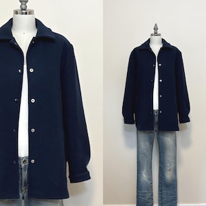 May include: A navy blue jacket with a button-up front and a collar, displayed on a mannequin. The jacket is paired with light blue jeans. The jacket has long sleeves and a classic design.