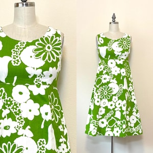 May include: A sleeveless A-line dress featuring a vibrant grass green background with a large-scale white floral pattern. The dress has a round neckline and a fitted bodice that transitions into a flared skirt, displaying a textured fabric finish.
