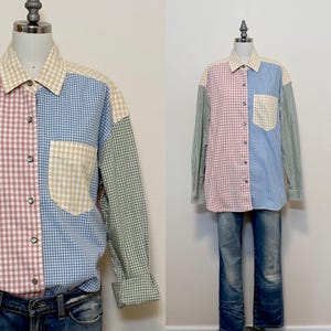 May include: A patchwork long-sleeved shirt with a button-down front. The shirt is made up of different gingham patterns in shades of pink, blue, green, and beige. It has a chest pocket and is worn with blue denim jeans.