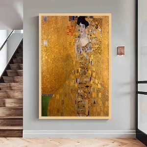 Puede incluir: Una impresión de arte mural enmarcada que muestra el retrato de una persona con cabello oscuro, vistiendo un vestido adornado con intrincados patrones de pan de oro, formas geométricas y motivos de ojos sobre un fondo dorado texturizado.