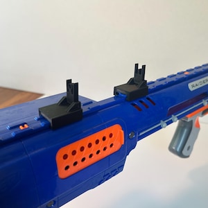May include: A blue and orange toy blaster with black plastic sights mounted on the top rail. The side of the blaster features a bright orange panel with circular perforations and the white text RAIDER CS-35 printed on the blue plastic body.