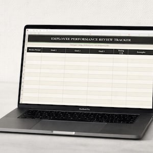 Puede incluir: Un ordenador portátil MacBook Pro plateado que muestra una hoja de cálculo "EMPLOYEE PERFORMANCE REVIEW TRACKER". La hoja de cálculo tiene columnas para el período de revisión, los objetivos, la calificación y las fortalezas. El portátil está abierto sobre una superficie blanca.