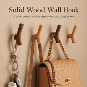 May include: Four solid wood wall hooks with a branch-inspired design mounted on a wall. The hooks are in varying shades of brown and light wood. One hook holds a keychain with a white charm, and another holds a tan quilted handbag with a gold chain.