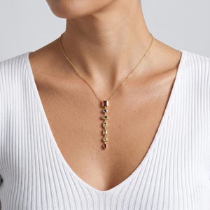 Puede incluir: Un collar de cadena dorada con un colgante vertical compuesto por siete piedras preciosas multicolores de diversas formas, incluyendo cortes cuadrados, redondos, ovalados y de pera, engastadas en oro en un patrón lineal descendente.