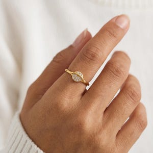 May include: A gold-toned ring featuring a circular centrepiece designed to resemble a planet with a surrounding ring. The circular face is embedded with multiple small, clear, sparkling stones arranged in a cluster across the surface.