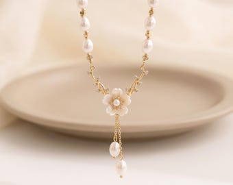 May include: A gold-tone necklace featuring a series of white oval pearls interspersed with small gold beads. The center pendant is a white flower with a pearl core, flanked by gold vine-like accents and two dangling pearl drops on gold chains.