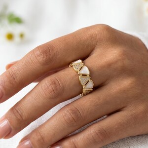 May include: A gold-toned ring featuring an alternating pattern of triangular white stone inlays and small, clear pavé-set crystals. The band is constructed from connected triangular segments, creating a geometric design that encircles the finger.