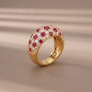 Könnte beinhalten: Ein goldener Kuppelring mit einer Pavé-Fassung aus abwechselnd rund geschliffenen roten Rubinen und klaren weißen Diamanten. Das Band hat eine glatte, polierte Goldoberfläche in der unteren Hälfte, während die obere Hälfte dicht mit Edelsteinen besetzt ist.