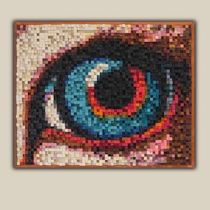 Puede incluir: Mosaico de madera enmarcado que representa un ojo detallado. El iris es una vibrante mezcla de azul, rojo y naranja, rodeado de negro y marrón. El mosaico está compuesto por pequeños bloques de madera cuadrados.