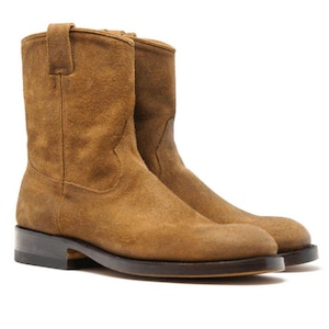 Könnte beinhalten: Ein Paar hellbraune Wildleder-Ankle Boots mit kleinem Absatz. Die Stiefel haben eine runde Spitze und eine Zuglasche am oberen Schaft. Die Sohlen sind dunkelbraun. Die Stiefel stehen vor einem weißen Hintergrund.