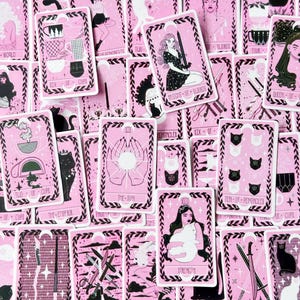 May include: A collection of tarot cards featuring a pink and black color scheme with various illustrations including cats, cups, swords, and figures. Each card displays distinct imagery and text labels such as The Sun, Strength, and Six of Cups.