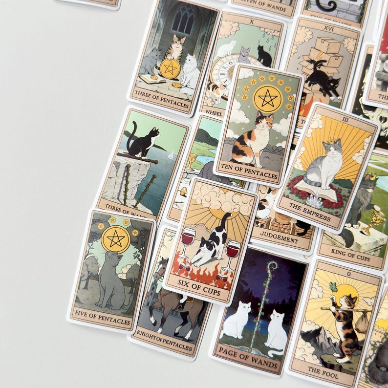May include: A collection of tarot cards featuring various cat illustrations. The cards include titles such as Three of Pentacles, Ten of Pentacles, The Empress, Six of Cups, Five of Pentacles, Knight of Pentacles, Page of Wands, and The Fool.