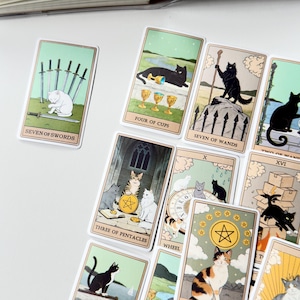 May include: A collection of tarot cards featuring cat illustrations. Visible cards include Seven of Swords, Four of Cups, Seven of Wands, Three of Pentacles, Wheel of Fortune, and others. Each card displays a cat in a scene with text labels.