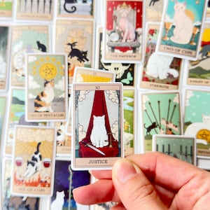 May include: A rectangular Justice tarot card sticker featuring a white cat with a blindfold sitting in front of a red curtain, holding a sword and scales. The card is bordered in cream with the Roman numeral XI and the text JUSTICE at the bottom.