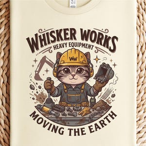 May include: Cream-colored t-shirt featuring a cartoon cat wearing a yellow hard hat and overalls, operating heavy equipment. The text "Whisker Works Heavy Equipment Moving the Earth" is arched above and below the cat illustration.