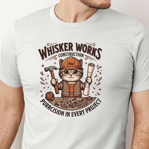 Puede incluir: Camiseta blanca con un gato de dibujos animados con casco y chaleco de trabajador de la construcci&oacute;n, sosteniendo un martillo y planos. El dise&ntilde;o incluye el texto "Whisker Works Construction" y "Purrcision in Every Project".