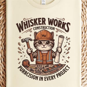 Puede incluir: Camiseta color crema con un gato de dibujos animados con un atuendo de trabajador de la construcci&oacute;n. El gato sostiene un martillo y un plano, con el texto "WHISKER WORKS CONSTRUCTION" y "PURRCISION IN EVERY PROJECT".