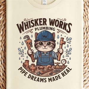 May include: Cream-colored t-shirt featuring a cartoon cat plumber wearing a blue hard hat and overalls, holding a wrench and pipe. The text "Whisker Works Plumbing" and "Pipe Dreams Made Real" are displayed in brown.
