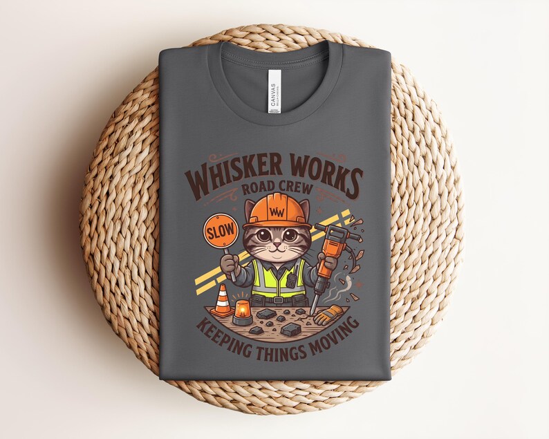 May include: Dark grey t-shirt with a cartoon cat in a construction worker outfit. The cat holds a "SLOW" sign and a jackhammer. Text on the shirt reads "WHISKER WORKS ROAD CREW KEEPING THINGS MOVING."