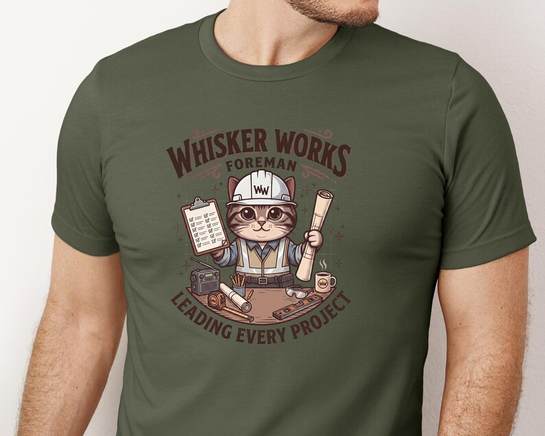 May include: Olive green t-shirt featuring a cartoon cat foreman wearing a hard hat and vest, holding blueprints and a clipboard. The text reads "Whisker Works Foreman Leading Every Project."