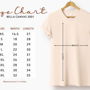 May include: A cream-colored t-shirt hanging on a wooden hanger. The image includes a size chart with measurements in inches for various sizes, from XS to 5XL. The text "Size Chart" and "BELLA CANVAS 3001" are visible.