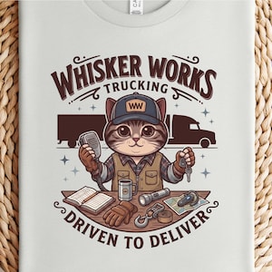 May include: A light grey t-shirt with a cartoon cat trucker design. The text reads "Whisker Works Trucking Driven to Deliver." The cat wears a cap and holds a microphone and keys. Other items include a mug, flashlight, and gloves.