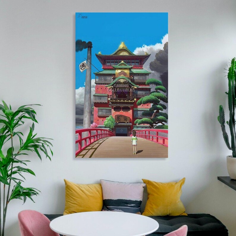 May include: A framed print of a scene from the animated film Spirited Away. The image features a red bridge leading to a large, ornate building with green and gold accents. The sky is blue with clouds, and the print has the text "GAMING COLLECTIBLES".