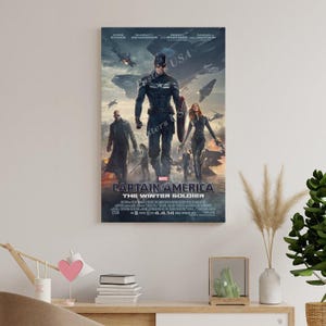Puede incluir: Un p&oacute;ster enmarcado de la pel&iacute;cula "Capit&aacute;n Am&eacute;rica: El Soldado de Invierno". El p&oacute;ster presenta al Capit&aacute;n Am&eacute;rica, otros personajes y aviones contra un cielo nublado. El t&iacute;tulo y la fecha de lanzamiento se muestran en la parte inferior.
