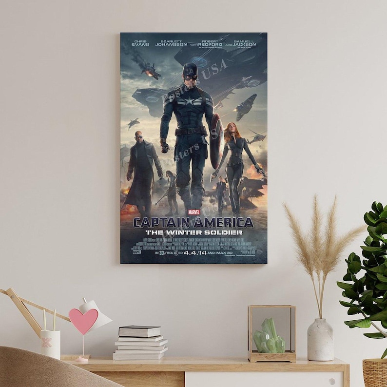 Puede incluir: Un p&oacute;ster enmarcado de la pel&iacute;cula "Capit&aacute;n Am&eacute;rica: El Soldado de Invierno". El p&oacute;ster presenta al Capit&aacute;n Am&eacute;rica, otros personajes y aviones contra un cielo nublado. El t&iacute;tulo y la fecha de lanzamiento se muestran en la parte inferior.