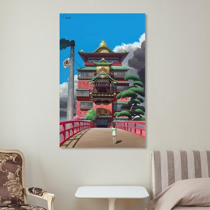 May include: A framed print of a scene from the animated film Spirited Away. The image features a red building with a bridge, a character walking, and the text "GAMING COLLECTIBLES". The sky is blue with clouds.