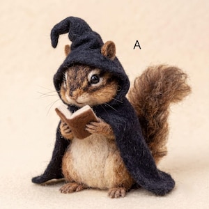 May include: A needle-felted chipmunk figurine wearing a dark navy blue hooded cloak and holding a small brown book. The chipmunk has brown and tan fur, a bushy tail, and the letter A is printed in black near the top right of the figure.