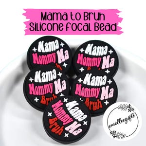 May include: A collection of black silicone focal beads with the words "Mama Mommy Ma Bruh" in white, pink, and red. The beads are round and have a plus sign and star design. The text "Mama to Bruh Silicone Focal Bead" is in a pink banner.
