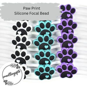 May include: Rows of silicone focal beads in paw print shapes. The beads are in white and black, teal and black, and purple and black. Each paw print has a heart in the center. The text "Paw Print Silicone Focal Bead" is at the top.