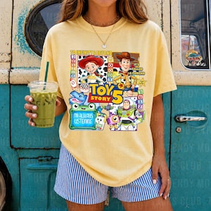 May include: A pale yellow short-sleeve t-shirt featuring a colorful Toy Story 5 graphic print. The design includes characters Jessie, Woody, and Buzz Lightyear, along with text that reads To Infinity & Beyond, Toy Story 5, and I'm Always Listening.
