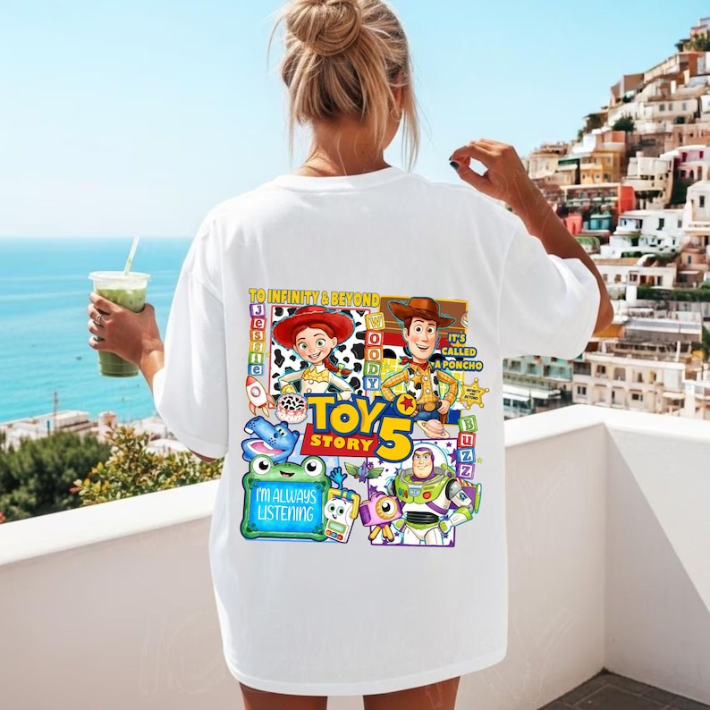 May include: A white t-shirt featuring a colorful graphic on the back with Toy Story characters including Jessie, Woody, and Buzz Lightyear. The design includes the text To Infinity & Beyond, Toy Story 5, and I'm Always Listening, along with various icons.