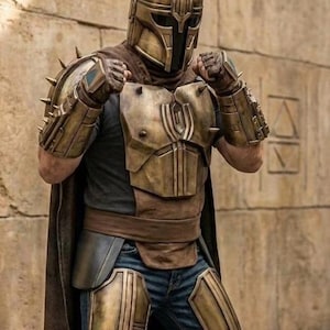 May include: A full-body suit of armor featuring a metallic bronze helmet with a T-shaped visor and spikes, matching shoulder pauldrons, gauntlets, and chest plate. The armor is worn over a dark shirt, blue jeans, and a long brown cape.