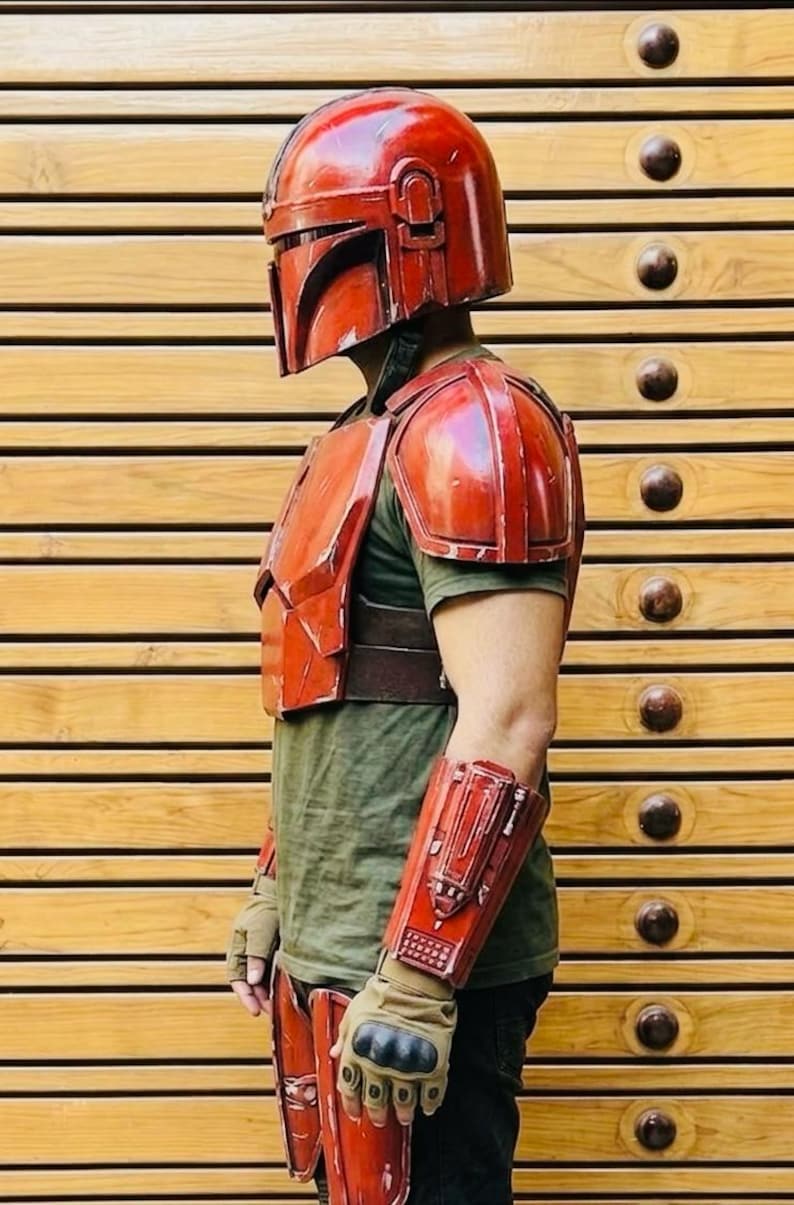 May include: Red Mandalorian armor set, including a helmet, chest plate, shoulder pads, arm guards, and leg armor. The armor is worn over a green shirt and brown belt. The gloves are tan and black.