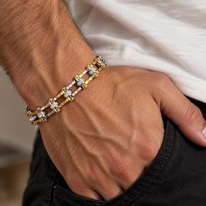 May include: A two-tone bracelet featuring a bicycle chain link design. The bracelet is constructed with alternating gold-toned and silver-toned metal links, creating a structured, mechanical appearance that wraps around the wrist.