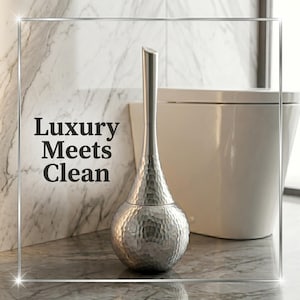 Könnte beinhalten: Eine silberne Toilettenbürste mit gehämmertem Muster, mit einem langen, schlanken Griff und einem abgerundeten Boden. Der Text "Luxury Meets Clean" ist in Schwarz dargestellt. Die Bürste befindet sich in einem modernen Badezimmer.