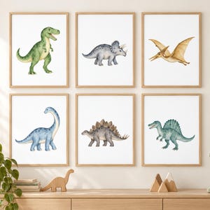May include: A set of six framed wall art prints featuring watercolor illustrations of dinosaurs. The collection includes a green Tyrannosaurus Rex, a grey Triceratops, a tan Pterodactyl, a blue Brachiosaurus, a grey Stegosaurus, and a green Spinosaurus.