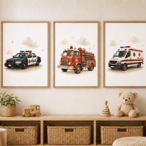Puede incluir: Un conjunto de tres láminas decorativas enmarcadas con ilustraciones en acuarela de vehículos de emergencia. La lámina izquierda muestra un coche de policía blanco y negro, la central un camión de bomberos rojo y la derecha una ambulancia.