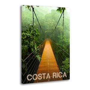 May include: A canvas print featuring a vibrant image of a suspension bridge in a lush, green rainforest. The bridge has a rusty orange metal walkway and is surrounded by dense foliage. The words "COSTA RICA" are printed in white at the bottom.