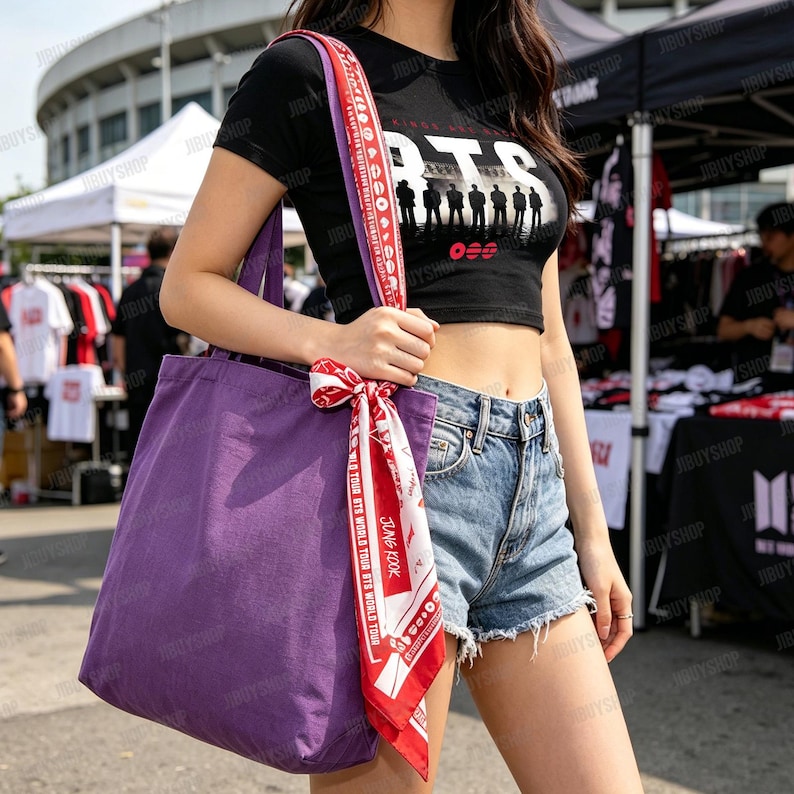 Peut inclure: Un sac fourre-tout violet avec une sangle &agrave; motifs rouges et blancs et un foulard assorti nou&eacute; &agrave; la poign&eacute;e. Le sac est port&eacute; &agrave; l'&eacute;paule. Un crop top noir avec le mot "BTS" et une silhouette de personnes est &eacute;galement visible.