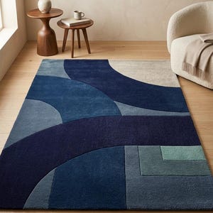 Esta alfombra presenta una sofisticada interacción de formas geométricas y una paleta de tonos fríos. Los arcos superpuestos y los rectángulos definidos crean