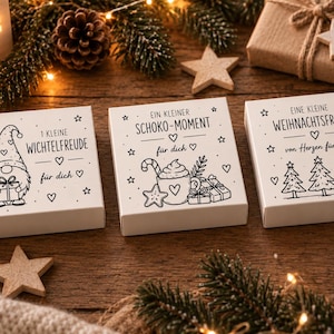 Könnte beinhalten: Drei weiße rechteckige Schachteln mit schwarzen Strichzeichnungen und deutschem Text. Die erste Schachtel zeigt einen Wichtel, die zweite eine Tasse mit Zuckerstange und die dritte drei Weihnachtsbäume. Jede Schachtel ist mit Sternen und Herzen verziert.