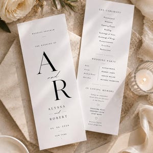 May include: Two white wedding programme cards with black serif typography. The front features the initials A and R, the names Alyssa and Robert, and the date 06-06-2026. The back lists the ceremony order, wedding party members, and a memorial section.