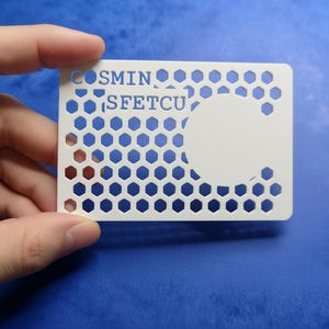 Puede incluir: Una tarjeta de visita blanca con un patrón de panal y el texto "COSMIN SFETCU". La tarjeta tiene un gran recorte circular y se sostiene sobre un fondo azul.