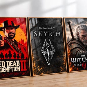 Puede incluir: Tres pósteres rectangulares enmarcados con ilustraciones de videojuegos. El póster de la izquierda muestra Red Dead Redemption II con un personaje sosteniendo un revólver. El póster central muestra el logotipo de The Elder Scrolls V Skyrim. El póster de la derecha representa The Witcher Wild Hunt.